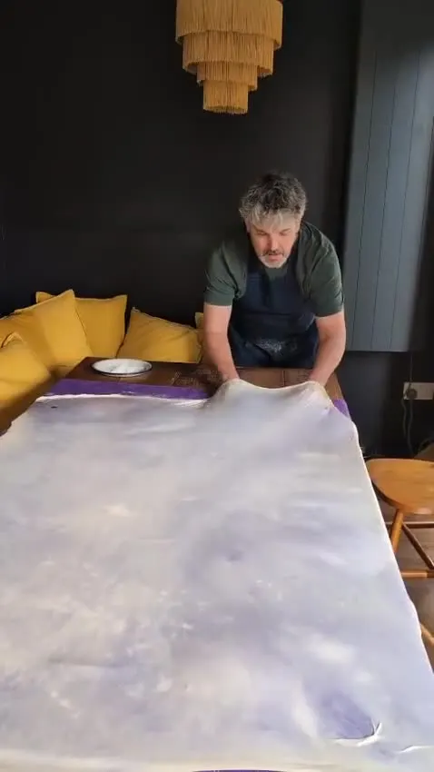 Dough being pulled across a kitchen table until it is paper thin