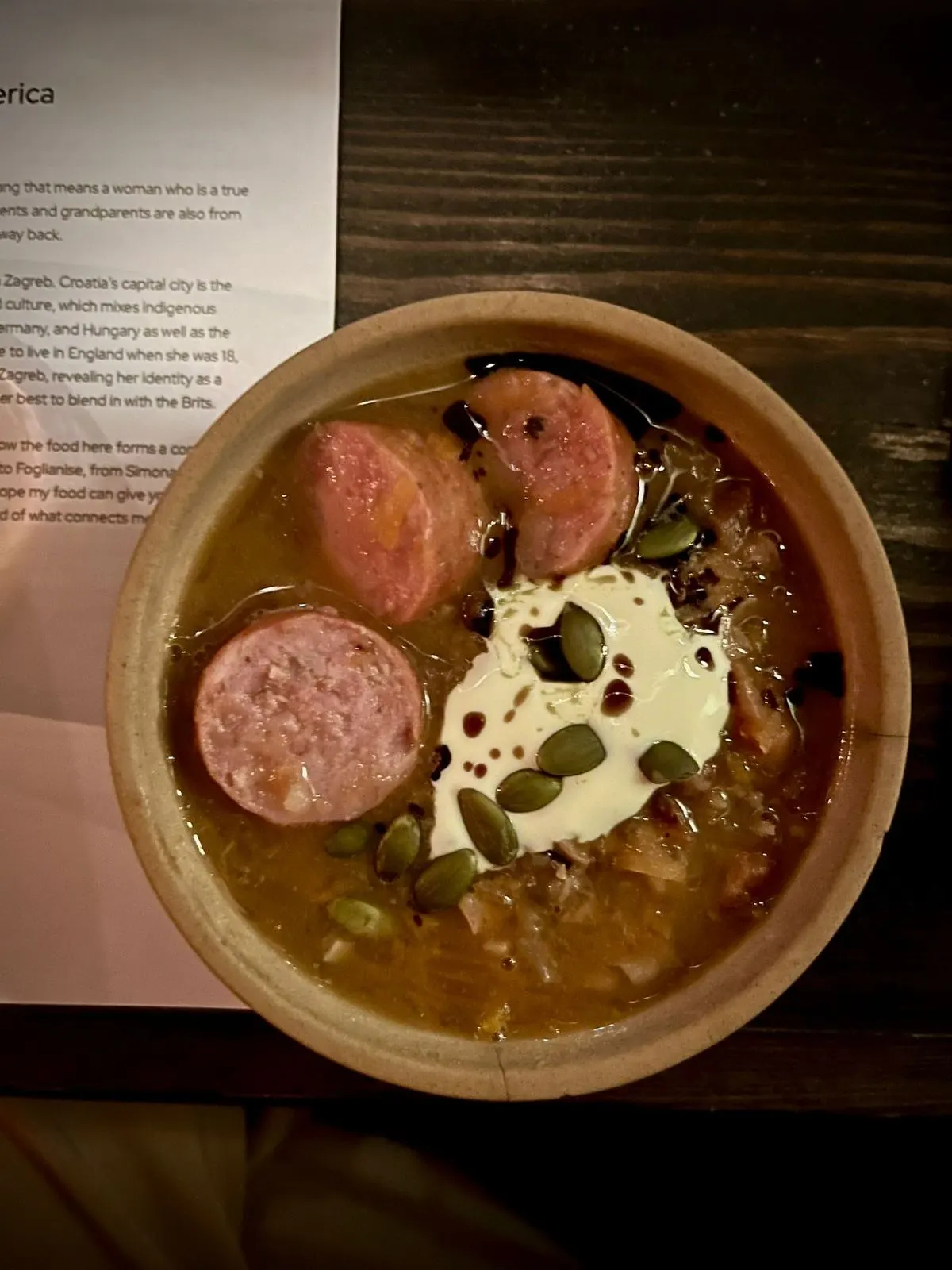 A bowl of bean soup with sliced sausage, sour cream and pumpkin seeds
